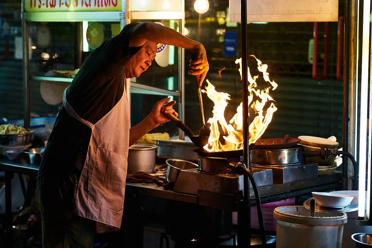 A street food stall cooking over open flame in Bangkok at night